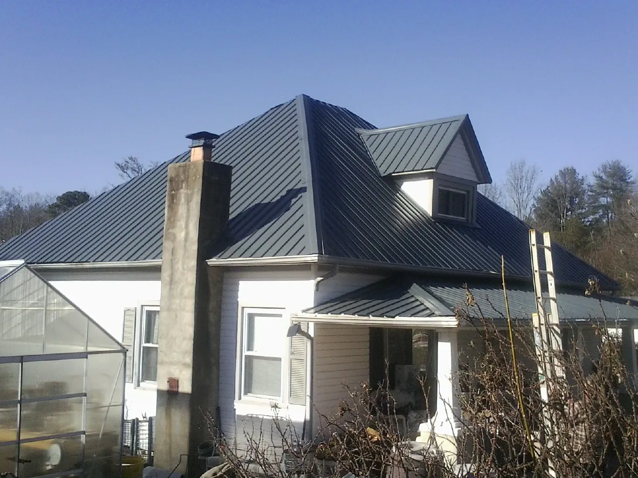 Dark blue standing seam metal roof on a white farmhouse with dormer — Slate & Tile Roof Repair by Roofing Brothers in Rhine