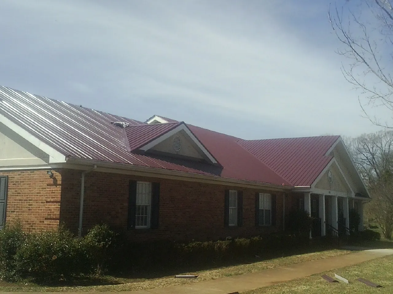 Red metal roof with gabled entries on a long brick building, from a Hail Damage Roof Repair job in Rhine