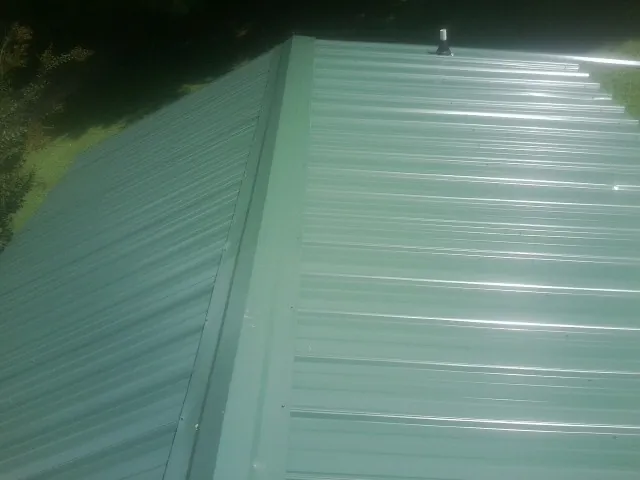 New green metal panels meeting at the ridge of a roof — Flat Roof Repair work by our crew in Rhine