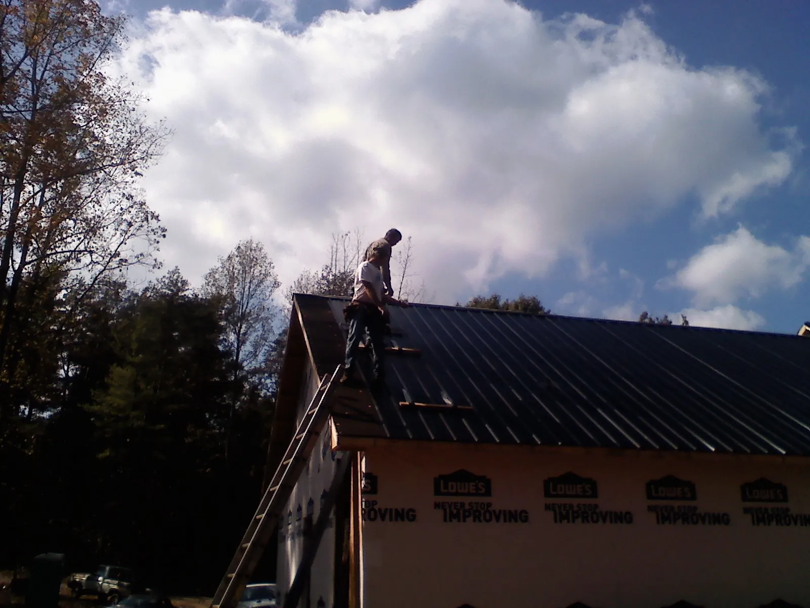 Roofer fastening dark metal panels high against a cloudy sky, from a Roof Inspection job in Rhine