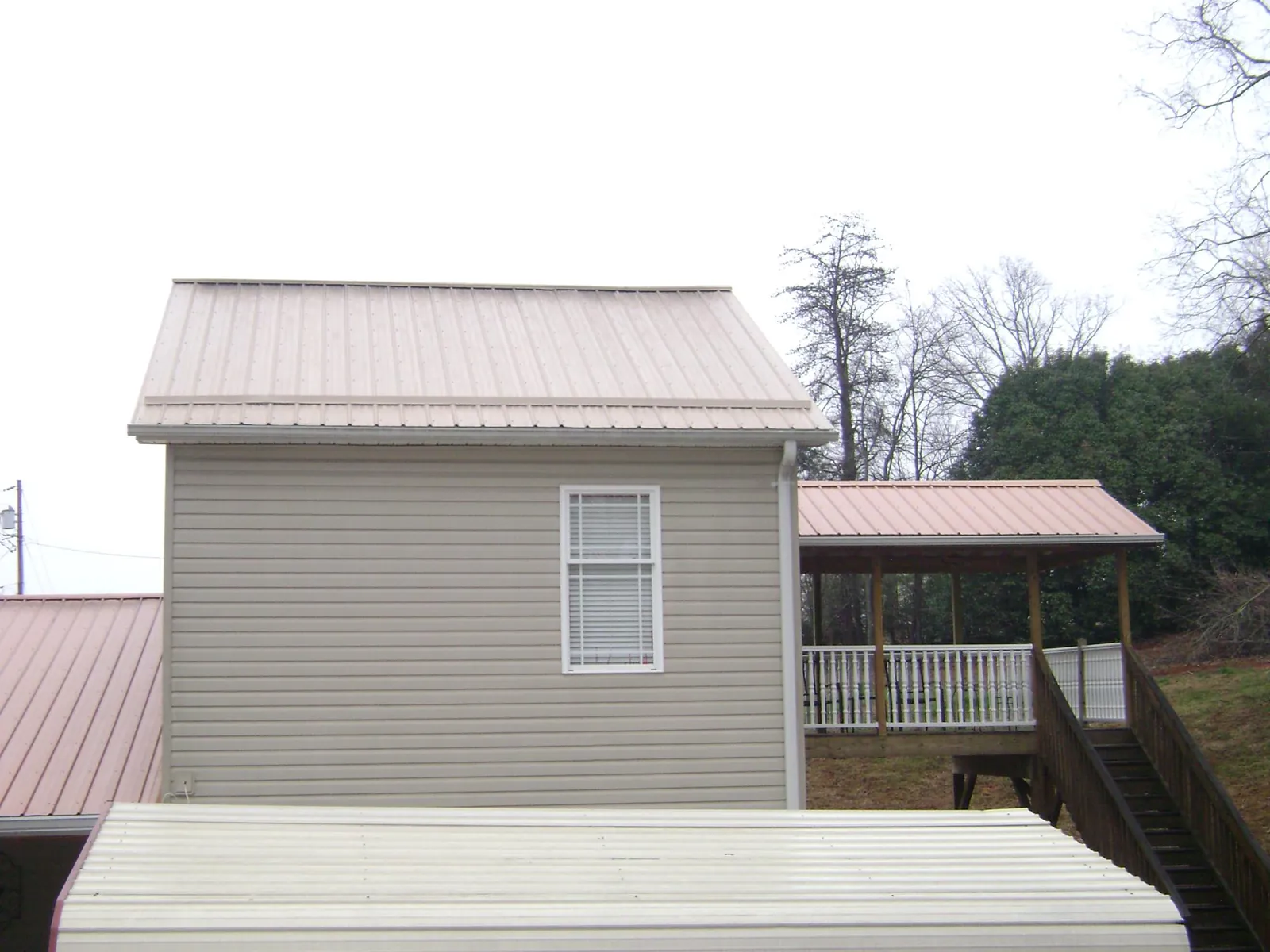 Tan metal roofs on a two story addition and attached porch, from a Roof Replacement job in Rhine